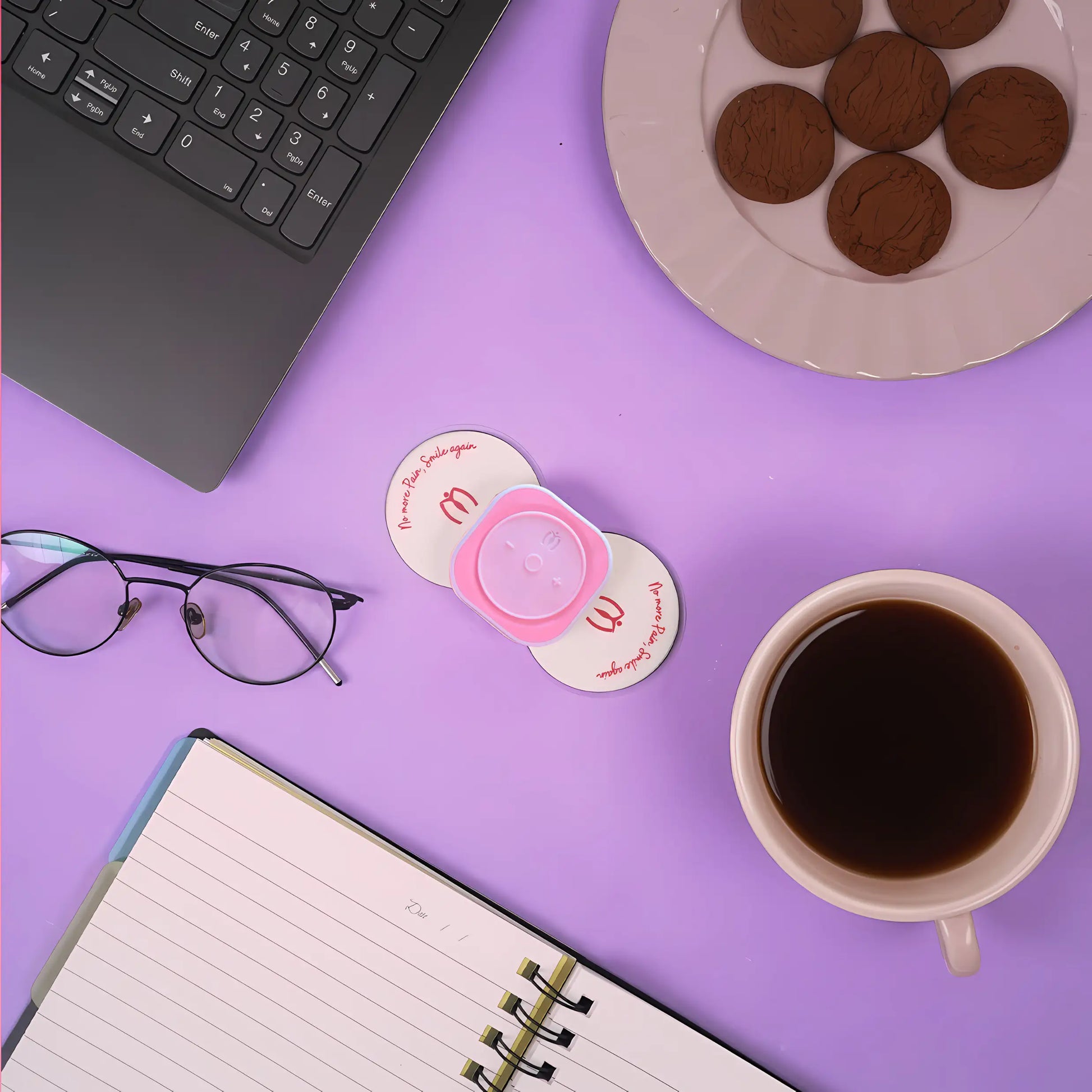 Matri, Purple desk with a laptop, coffee cup, notebook, glasses, and cookies on a purple surface.